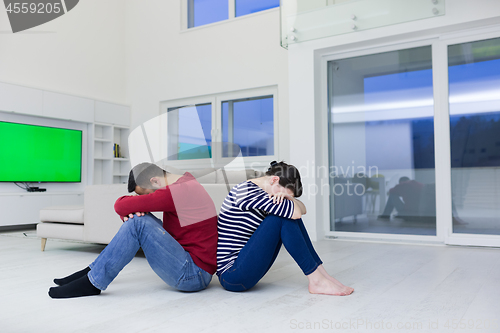 Image of young couple sitting with back to each other on floor