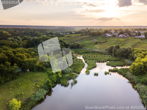 Image of Beautiful countryside landscape with village, forest, fields, river against summer cloudy sky at sunset.