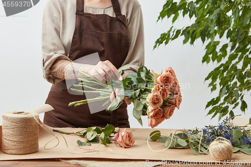 Image of Female florist making beautiful bouquet from living coral color roses on a light background. Process step by step