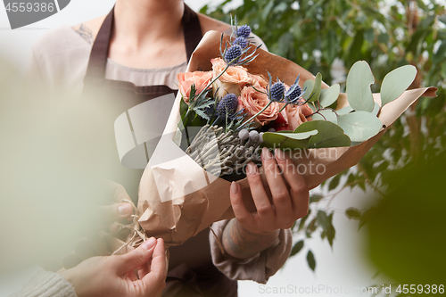 Image of Close-up of roses flowers bouquet in a woman\'s hands on a blured green leaf background.