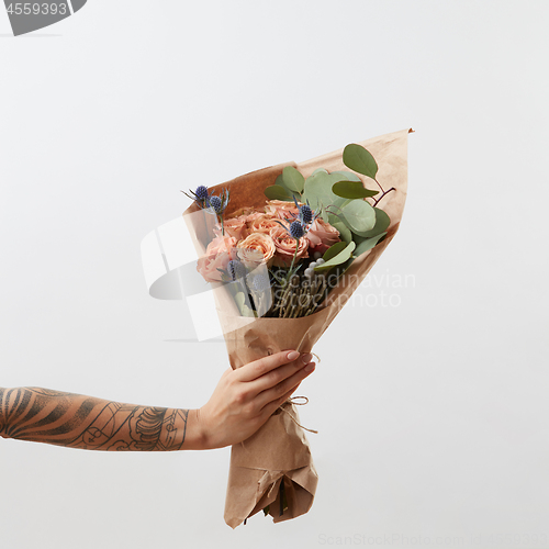 Image of Delicate flowers living coral roses and eryngium as a beautiful bouquet in girl\'s hand with tattoo, copy space. Congratulation card.