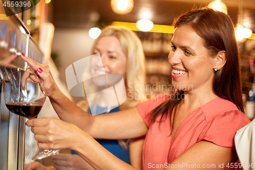 Image of happy women pouring wine from dispenser at bar