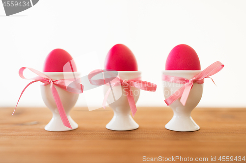 Image of three pink colored easter eggs in holders on table