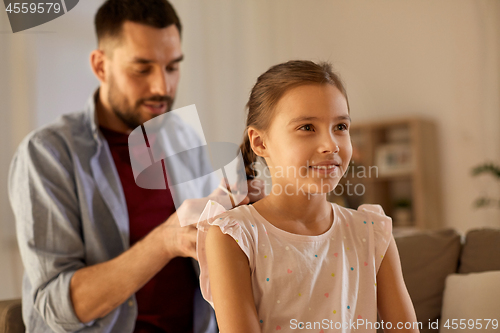 Image of father braiding daughter hair at home