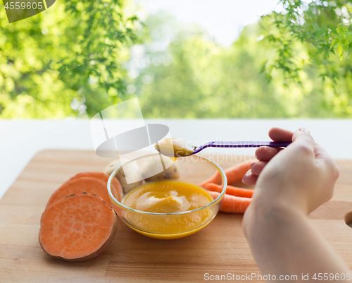 Image of hand with vegetable puree or baby food in spoon