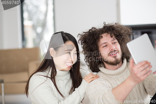 Image of multiethnic couple using tablet computer in front of fireplace