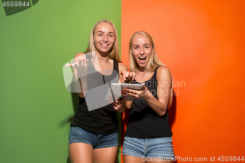 Image of Picture of two young happy women looking at the camera and holding laptop.