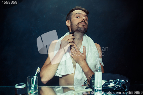 Image of young man in bedroom sitting in front of the mirror scratching his beard