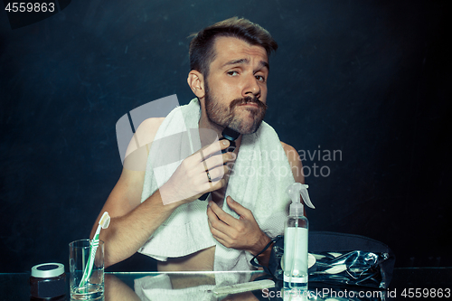 Image of young man in bedroom sitting in front of the mirror scratching his beard