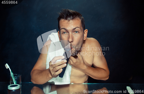 Image of young man in bedroom sitting in front of the mirror scratching his beard