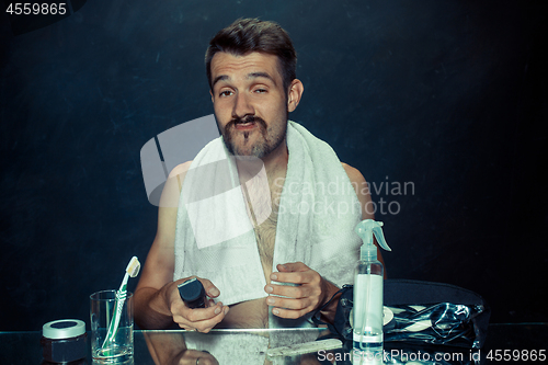 Image of young man in bedroom sitting in front of the mirror scratching his beard