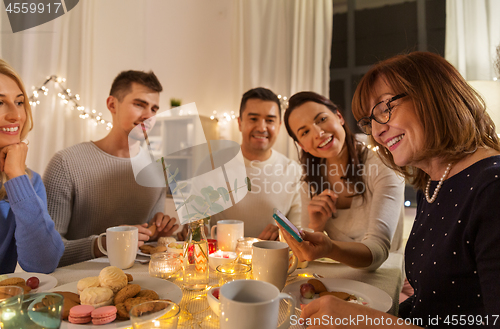 Image of happy family with smartphone at tea party at home