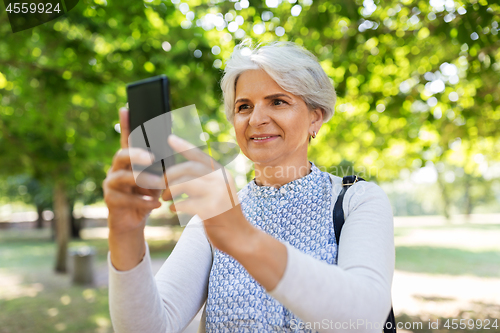 Image of senior woman photographing by cell at summer park