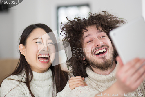 Image of multiethnic couple using tablet computer in front of fireplace