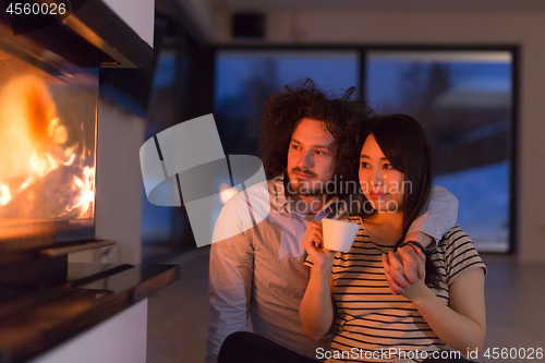 Image of happy multiethnic couple sitting in front of fireplace