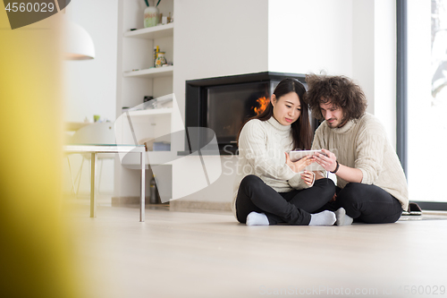 Image of multiethnic couple using tablet computer in front of fireplace