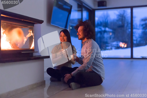 Image of happy multiethnic couple sitting in front of fireplace