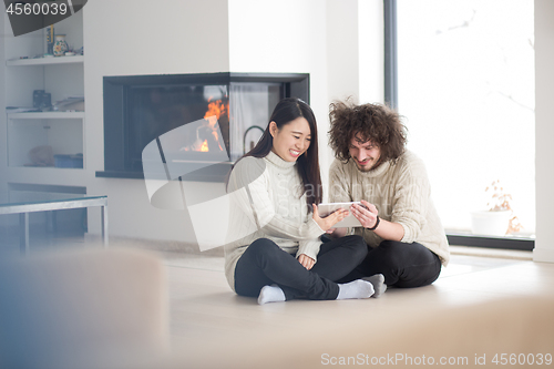 Image of multiethnic couple using tablet computer in front of fireplace