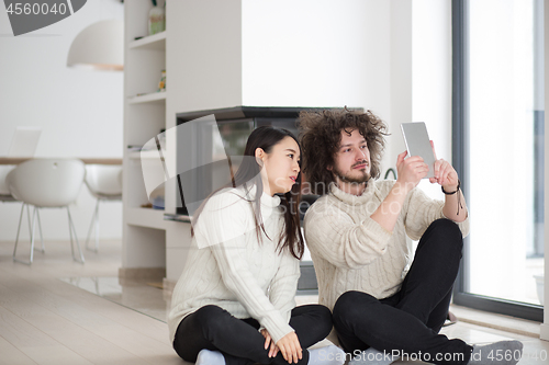 Image of multiethnic couple using tablet computer in front of fireplace