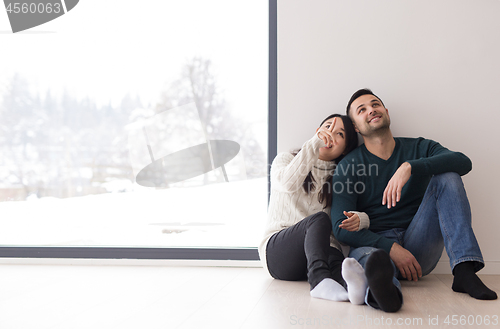 Image of multiethnic couple sitting on the floor near window at home