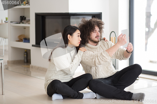 Image of multiethnic couple using tablet computer in front of fireplace