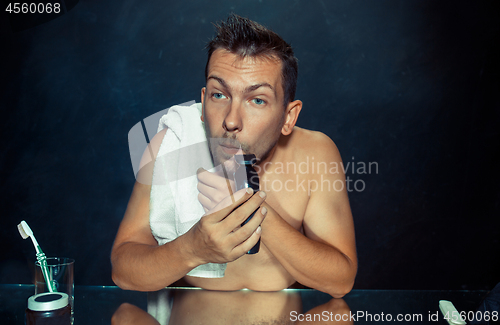 Image of young man in bedroom sitting in front of the mirror scratching his beard