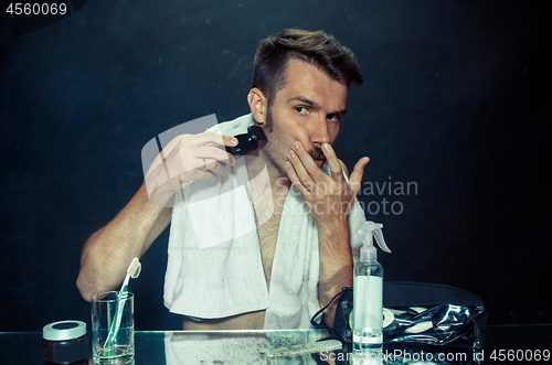 Image of young man in bedroom sitting in front of the mirror scratching his beard