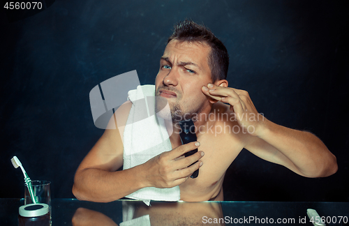 Image of young man in bedroom sitting in front of the mirror scratching his beard