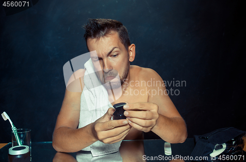 Image of young man in bedroom sitting in front of the mirror scratching his beard