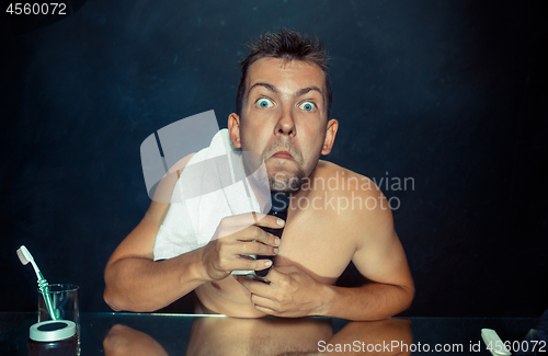 Image of young man in bedroom sitting in front of the mirror scratching his beard