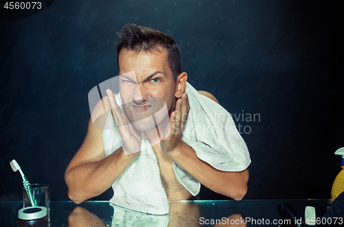 Image of young man in bedroom sitting in front of the mirror scratching his beard