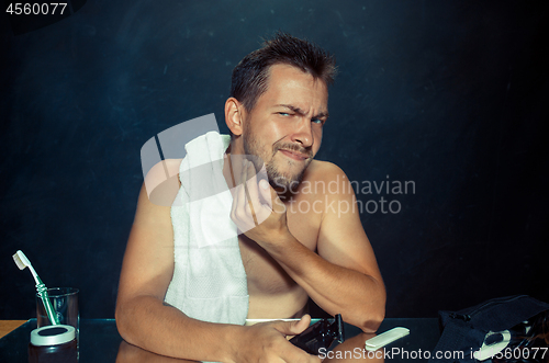 Image of young man in bedroom sitting in front of the mirror scratching his beard