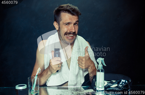 Image of young man in bedroom sitting in front of the mirror scratching his beard