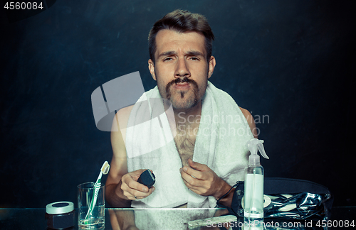 Image of young man in bedroom sitting in front of the mirror scratching his beard