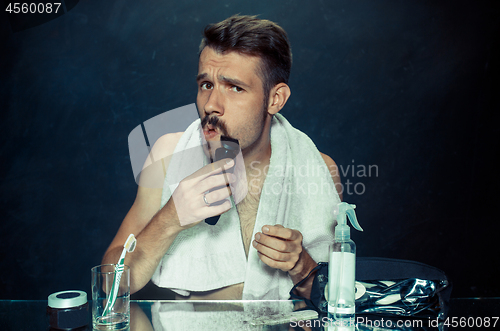 Image of young man in bedroom sitting in front of the mirror scratching his beard