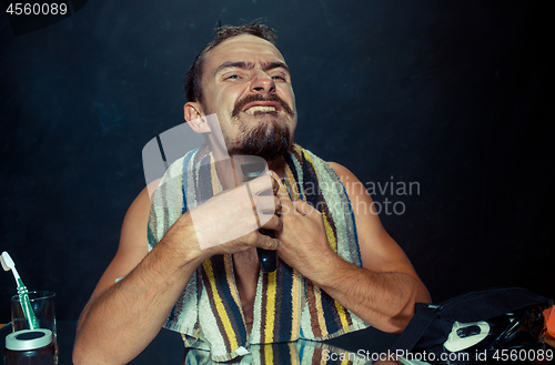 Image of young man in bedroom sitting in front of the mirror scratching his beard