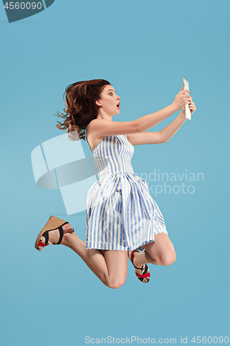 Image of Image of young woman over blue background using laptop computer or tablet gadget while jumping.