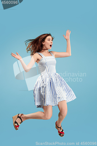 Image of Freedom in moving. Pretty young woman jumping against blue background