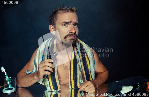 Image of young man in bedroom sitting in front of the mirror scratching his beard