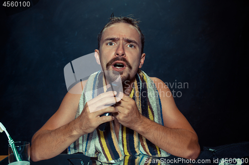 Image of young man in bedroom sitting in front of the mirror scratching his beard