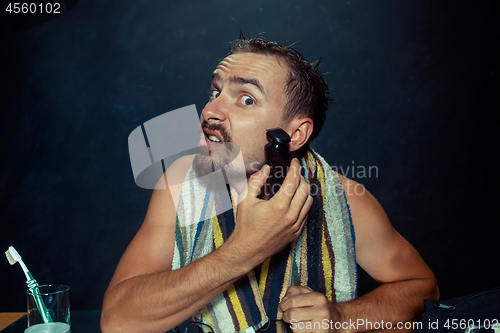 Image of young man in bedroom sitting in front of the mirror scratching his beard