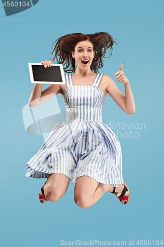 Image of Image of young woman over blue background using laptop computer or tablet gadget while jumping.