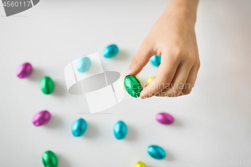 Image of hand of child with chocolate easter eggs in foil