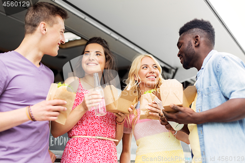 Image of happy friends with drinks eating at food truck