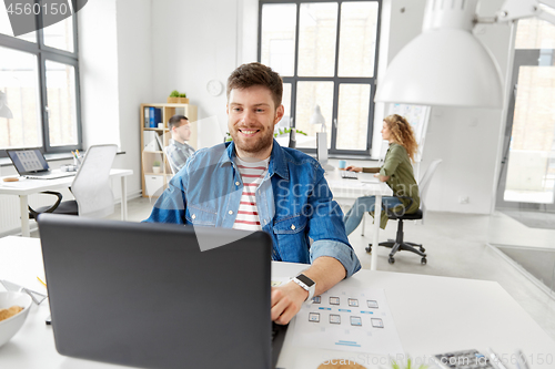 Image of smiling creative man with laptop working at office