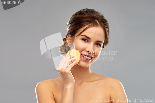 Image of young woman cleaning face with exfoliating sponge