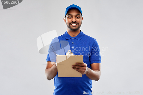 Image of happy indian delivery man with clipboard in blue