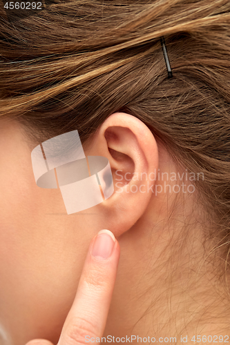 Image of close up of young woman pointing finger to her ear