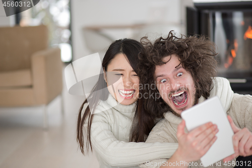 Image of multiethnic couple using tablet computer in front of fireplace