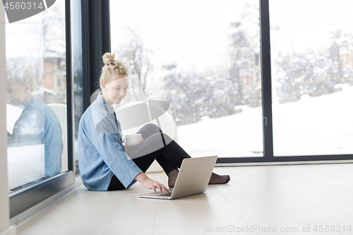 Image of woman drinking coffee and using laptop at home
